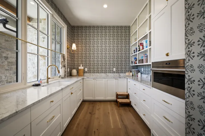 Custom built-in cabinetry with brass hardware, undermount sink with brass faucet, stone countertops, wood-finish flooring, and integrated wall oven
