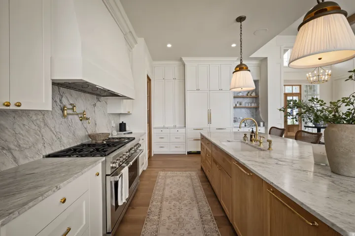 Gourmet kitchen featuring a large central island with seating, a range with a pot filler, extensive white cabinetry, brass hardware, and stone countertops