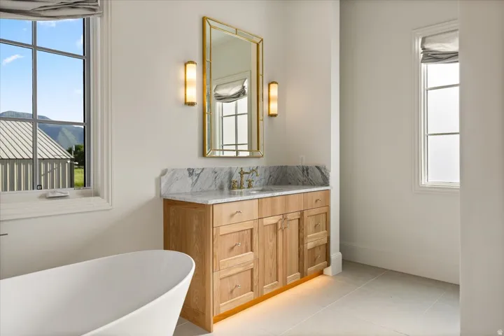 Freestanding soaking tub with a light wood-finish vanity, marble countertop, and gold-framed mirror