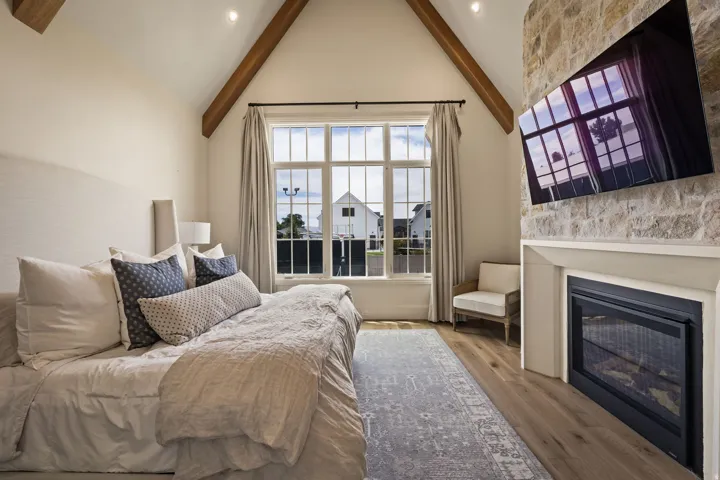 Vaulted ceilings with exposed wood beams, large multi-pane window, built-in fireplace with stone surround, wood-finish flooring, and recessed lighting