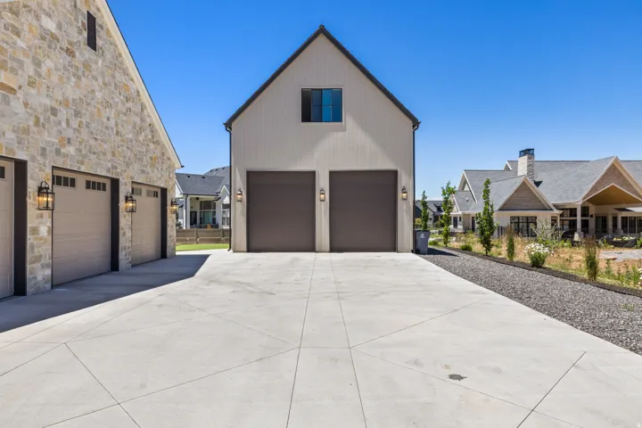Expansive concrete driveway with geometric scoring, providing access to a three-car garage with carriage-style doors and a separate two-car garage
