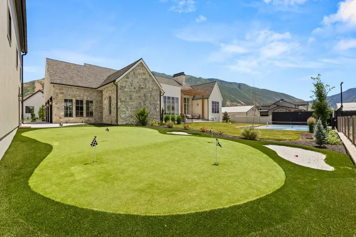 Expansive backyard featuring a multi-hole putting green with sand trap, integrated artificial turf, stone exterior, and a mountain backdrop
