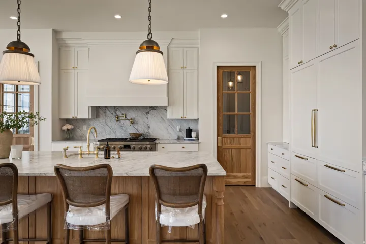 Gourmet kitchen featuring a substantial island with stone countertop, integrated range with pot filler, full-height stone backsplash, and custom cabinetry with brass hardware