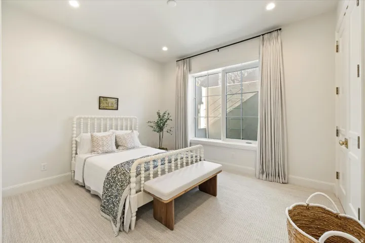 Recessed lighting illuminates a space featuring a large window with white casing and light-toned drapery