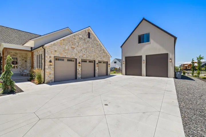 Expansive concrete driveway with geometric scoring leading to a stone facade residence and a separate board-and-batten auxiliary building