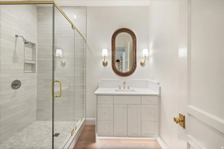 Bathroom featuring a glass-enclosed shower with subway tile surround and hexagonal floor tiles, a single vanity with a white countertop and undermount sink, a framed oval mirror, and brass-finish fixtures and hardware