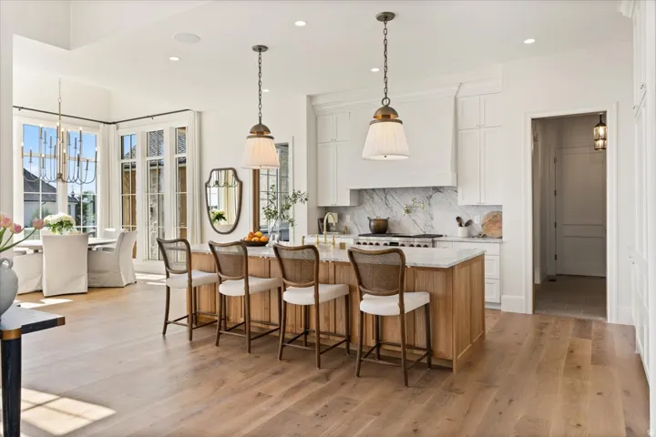 Spacious kitchen featuring a large wood-finish island with seating, white shaker cabinetry, marble backsplash, and dual pendant lighting