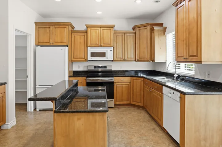 Kitchen featuring wood cabinetry, dark countertops, an island with a breakfast bar, stainless steel appliances, and a pantry with shelving