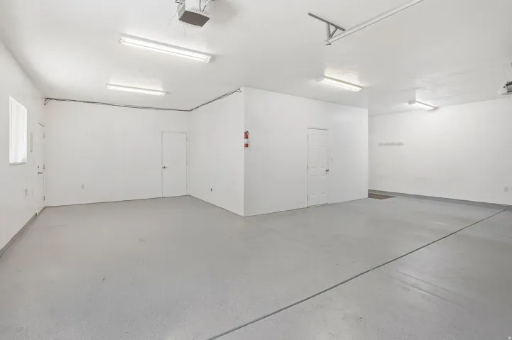 Spacious garage featuring a light gray epoxy floor coating, multiple fluorescent lighting fixtures, and direct access doors