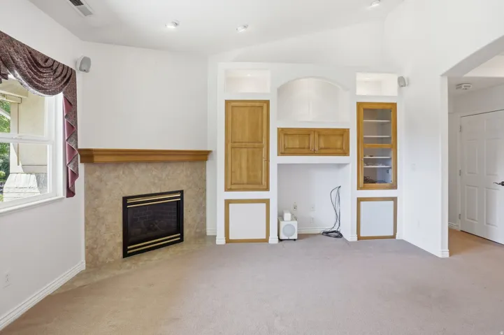 Living area featuring a corner fireplace with a tiled surround and wood mantel, built-in cabinetry with wood-finish doors and shelving, a window with exterior views, and recessed lighting