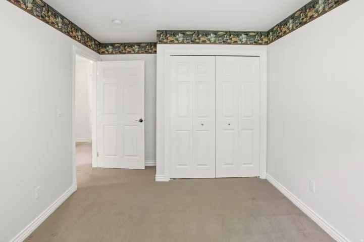 Neutral tone walls with a decorative wallpaper border, carpet flooring, a white paneled door, and bi-fold closet doors