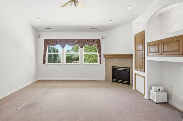 Spacious room featuring a fireplace with a stone surround and wood mantel, built-in cabinetry, recessed lighting, and a ceiling fan