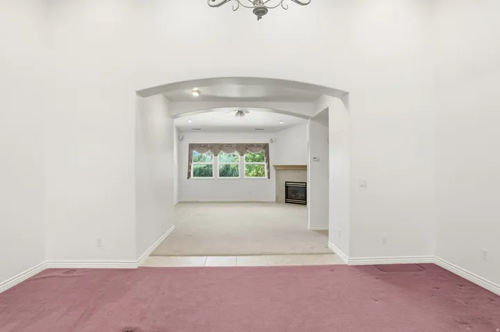 Archway entry from a carpeted room into a living space featuring a fireplace with a stone surround, multiple windows, and a ceiling fan