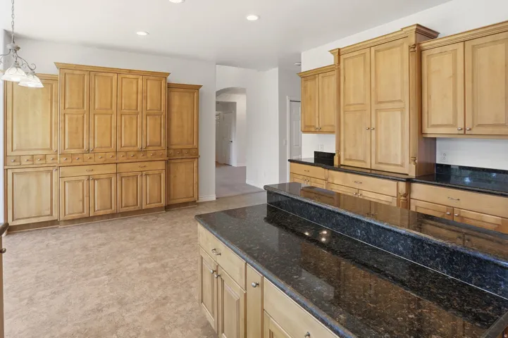 Expansive kitchen featuring abundant wood cabinetry, dark granite countertops, a large center island, built-in pantry storage, and recessed lighting