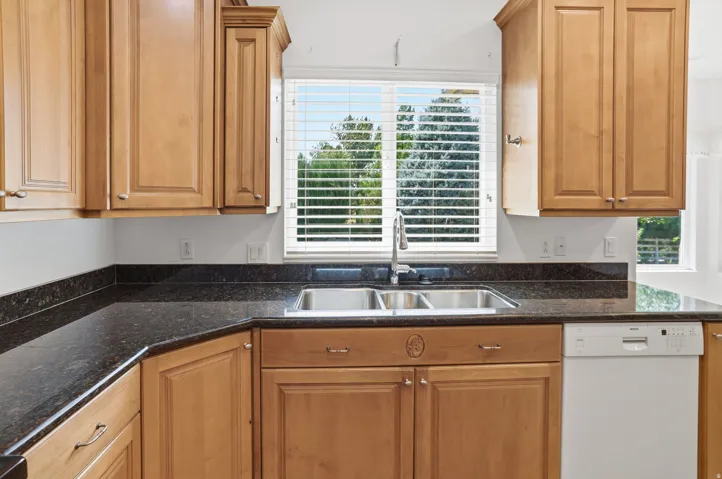 Kitchen featuring a stainless steel double sink, granite countertops, wood-finish cabinetry, and a built-in dishwasher