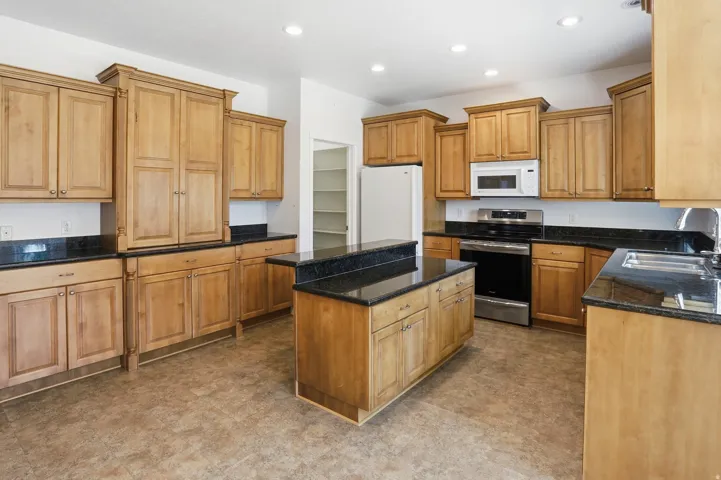 Kitchen with natural wood cabinetry, dark countertops, and stainless steel appliances