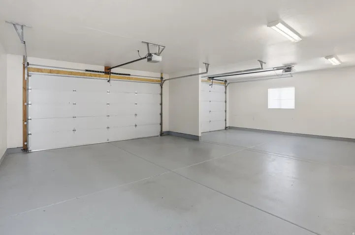 Spacious garage featuring two overhead doors, a window, concrete flooring, and fluorescent lighting