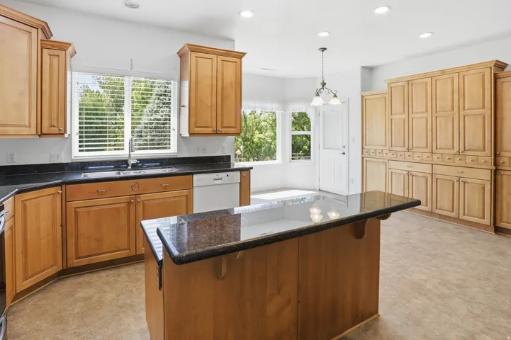 Kitchen featuring wood cabinetry, dark countertops, a central island with countertop seating, and recessed lighting