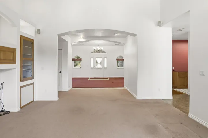 Archway entry into a spacious interior featuring light-colored carpeting, a built-in display cabinet with glass doors, and recessed lighting