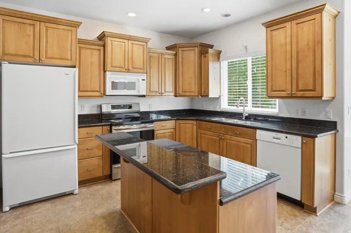 Kitchen featuring granite countertops, wood cabinetry, stainless steel range, and a central island