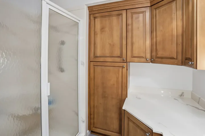 Walk-in shower with textured glass enclosure, complemented by extensive wood cabinetry and a white countertop
