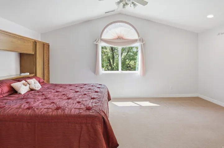Vaulted ceiling bedroom featuring a large arched window, built-in wooden cabinetry, recessed lighting, and a ceiling fan