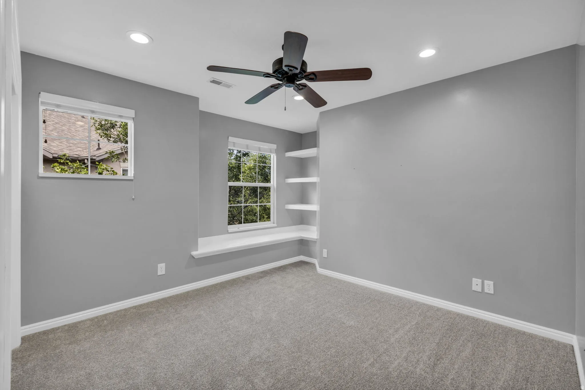 Spacious room featuring neutral carpeting, recessed lighting, a ceiling fan, and built-in corner shelving
