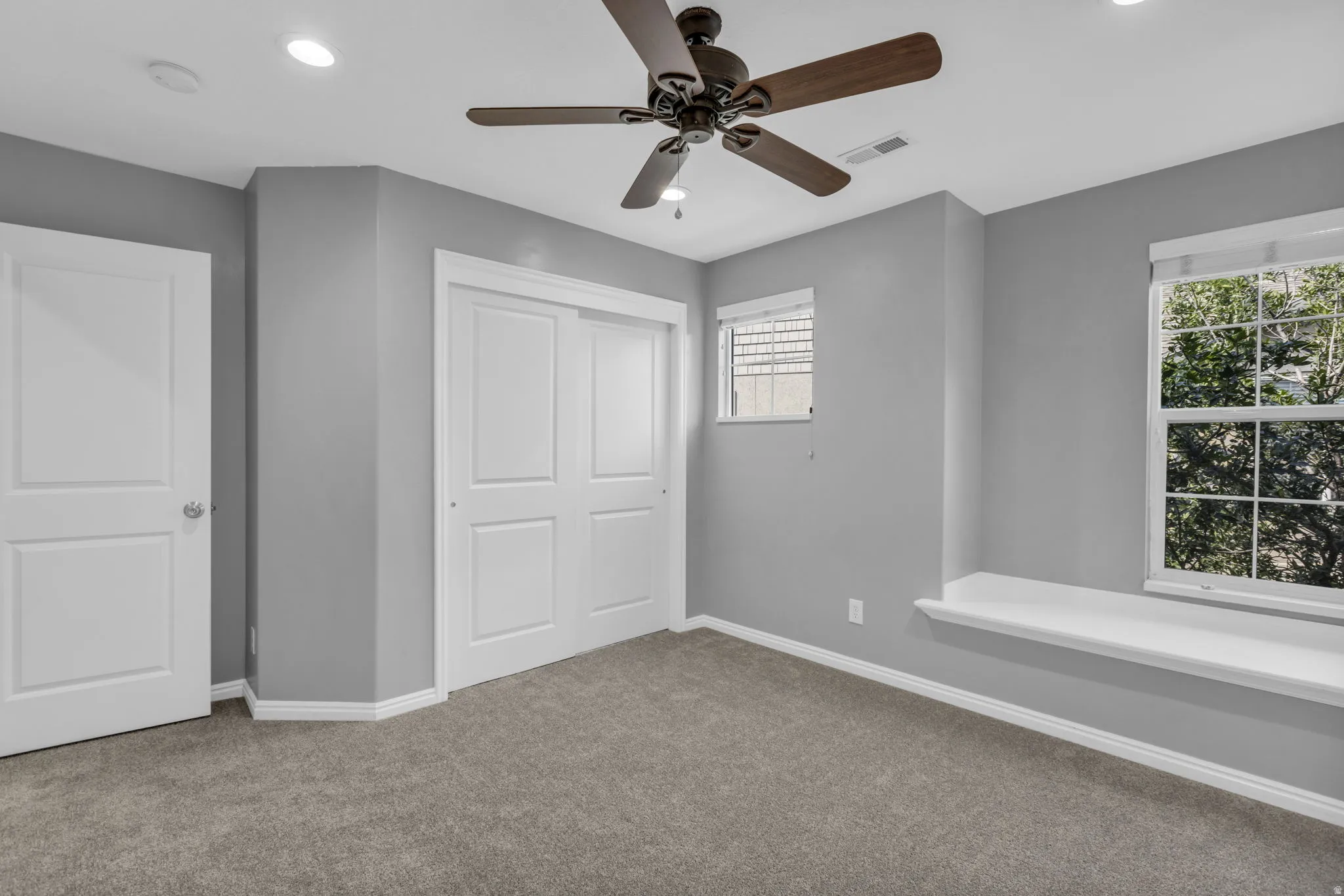 Spacious room with plush gray carpeting, recessed ceiling lighting, and a dark-toned ceiling fan