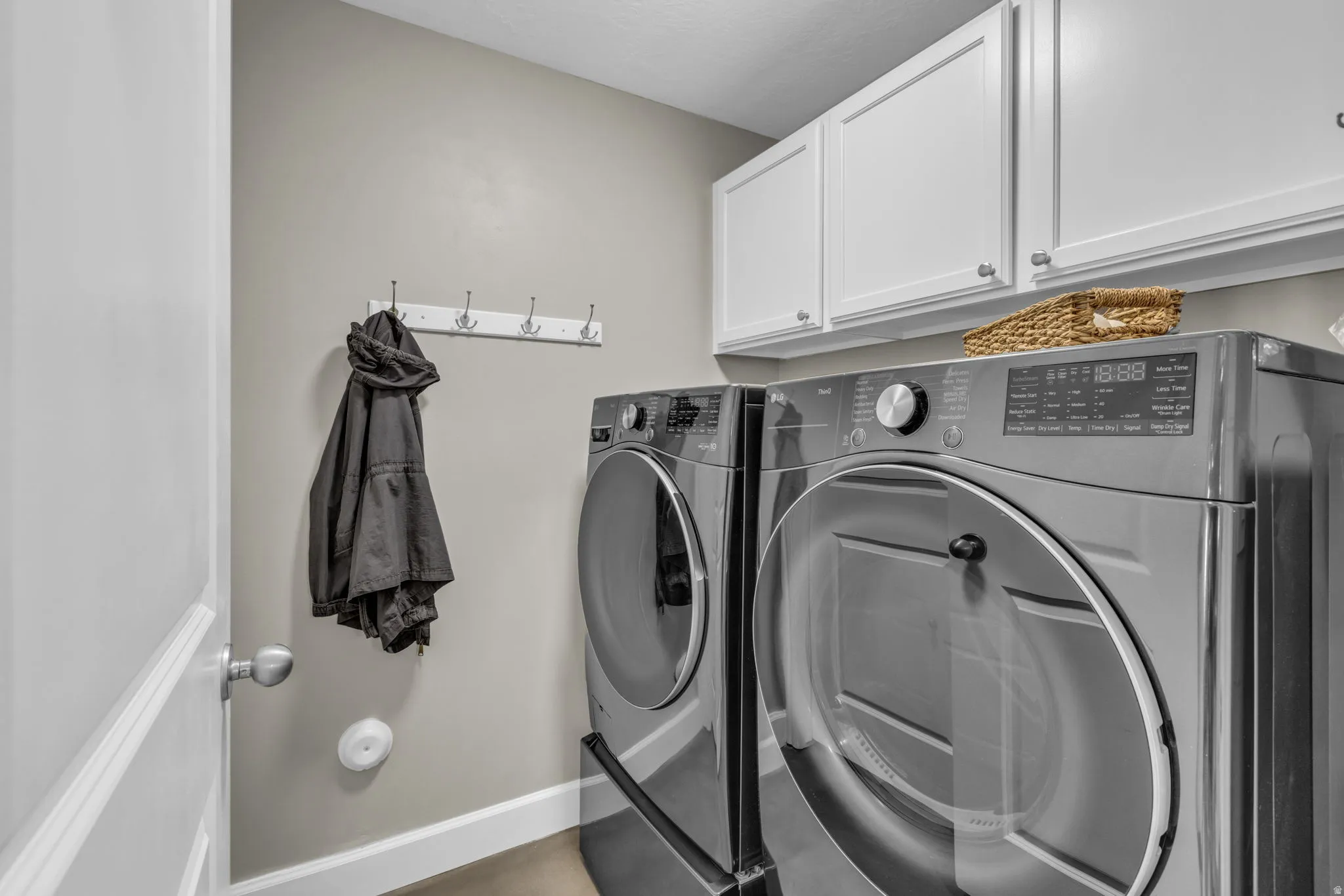 Dedicated laundry area featuring white upper cabinetry, a mounted coat rack, light gray walls, and white baseboards