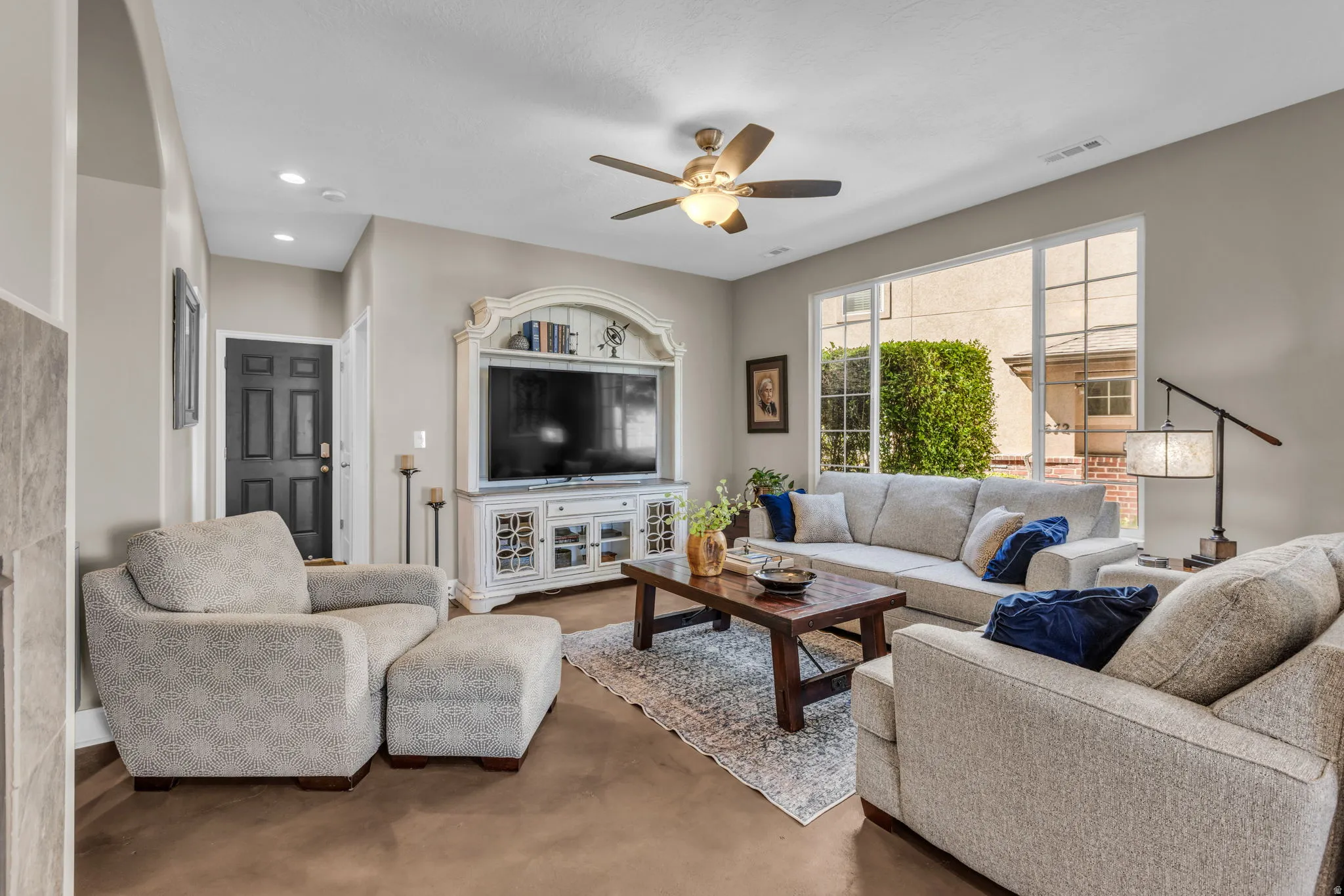 Spacious living area featuring light-toned walls, recessed lighting, a ceiling fan, and large windows providing natural light