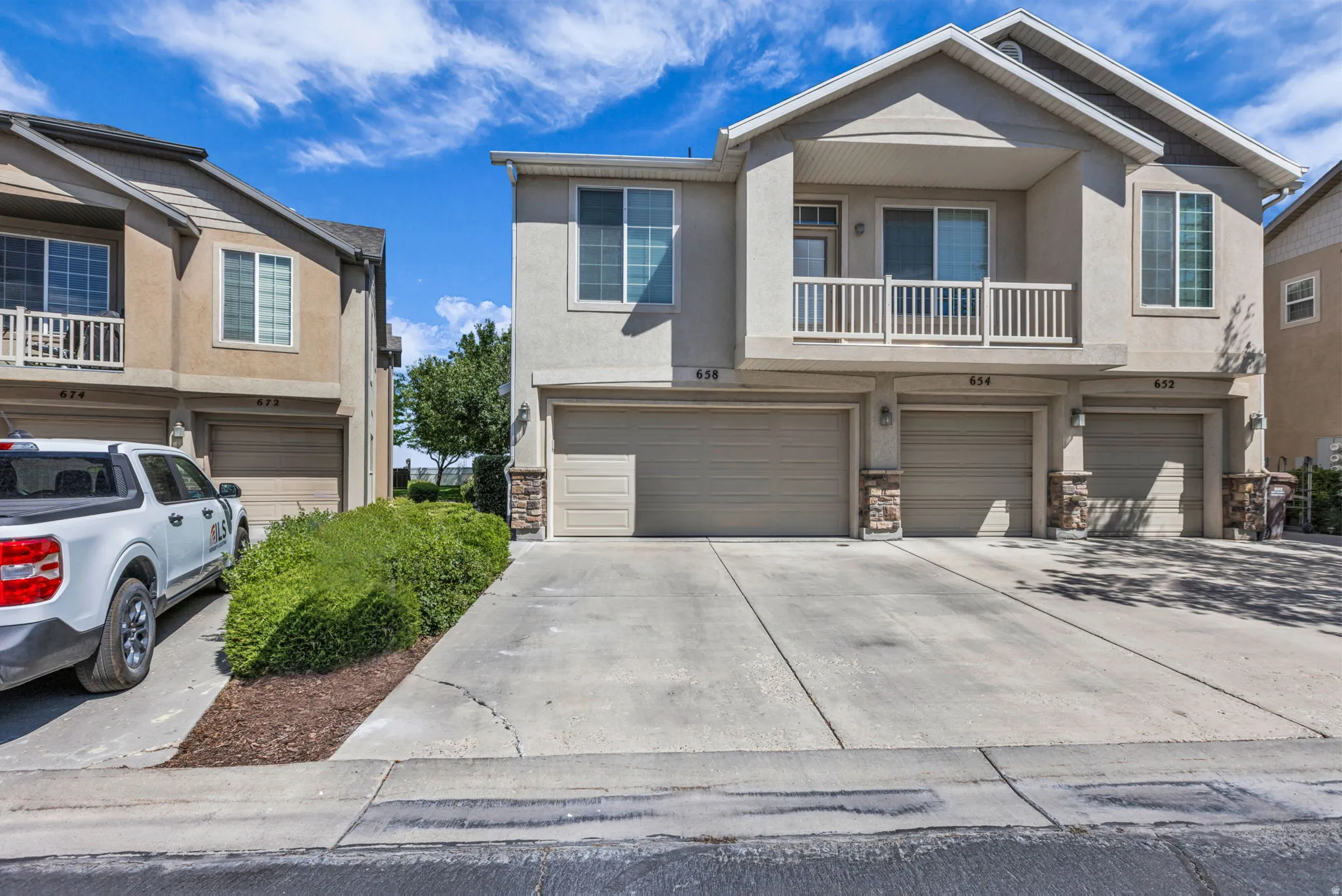 Stucco exterior building featuring multiple garage bays, stone accents, and a second-story balcony with white railing