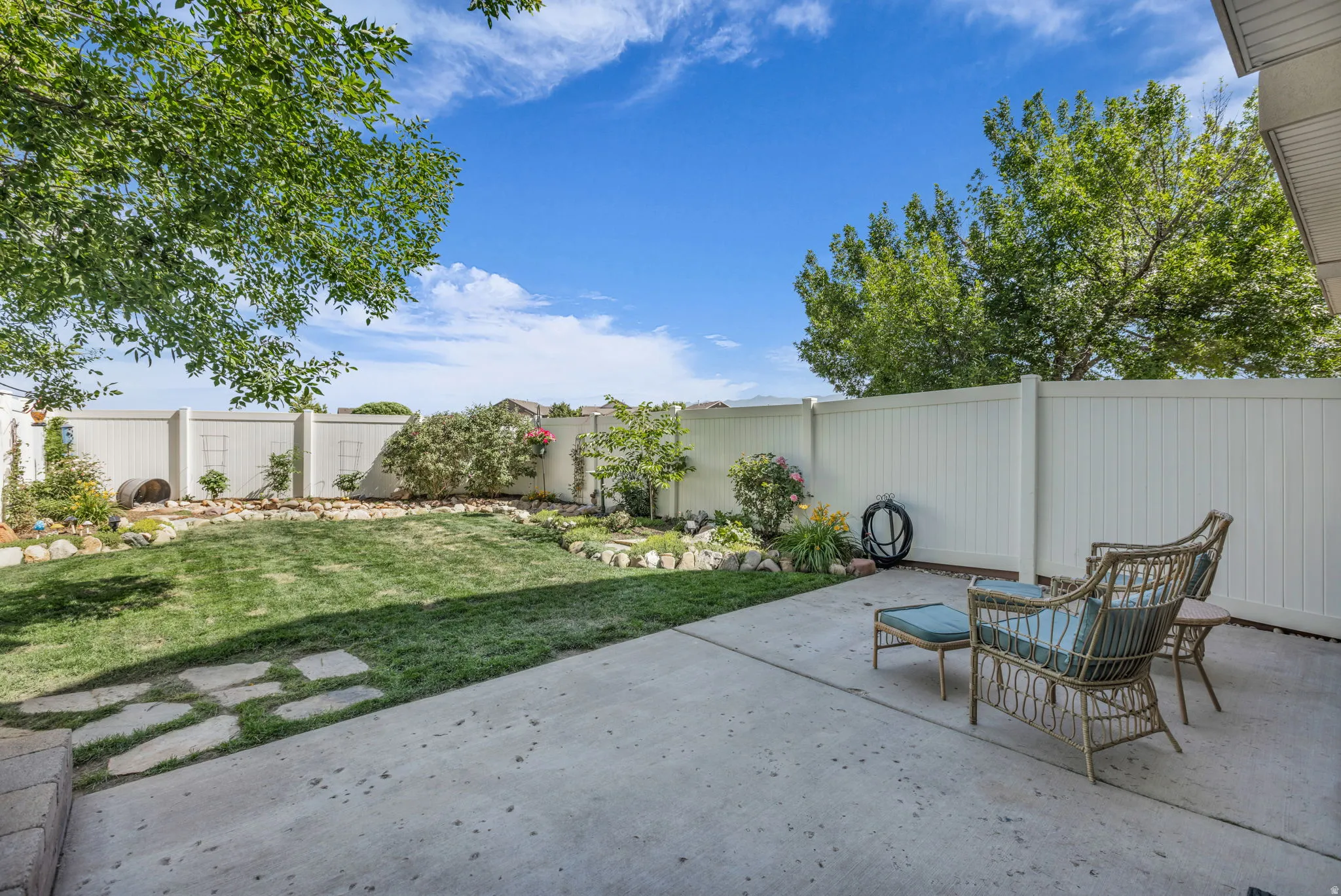 Private backyard featuring a concrete patio, expansive lawn, stone-edged landscaping beds, and a perimeter privacy fence