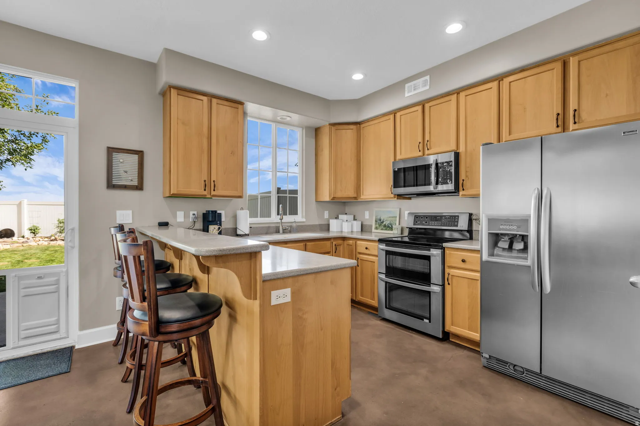 Kitchen with light wood cabinetry, stainless steel appliances, recessed lighting, and a peninsula with countertop seating