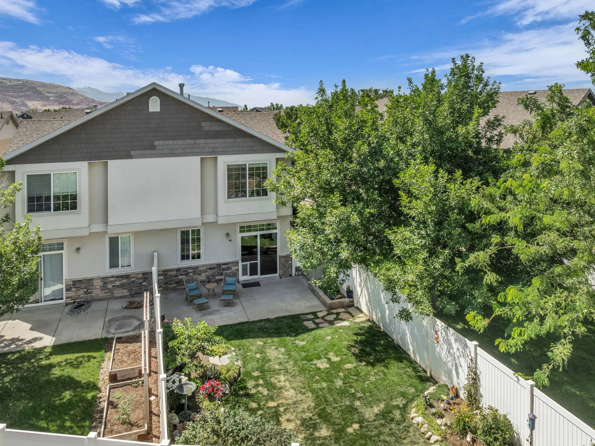Rear exterior featuring a spacious concrete patio, multi-level raised garden beds, and a manicured lawn