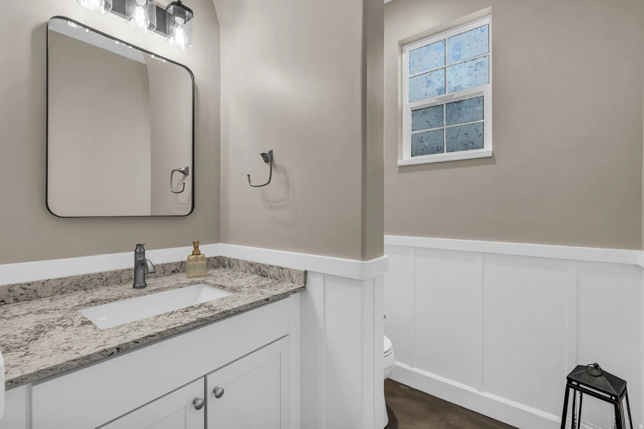 Vanity featuring a stone-finish countertop with an undermount sink, a rectangular framed mirror, and a three-light fixture