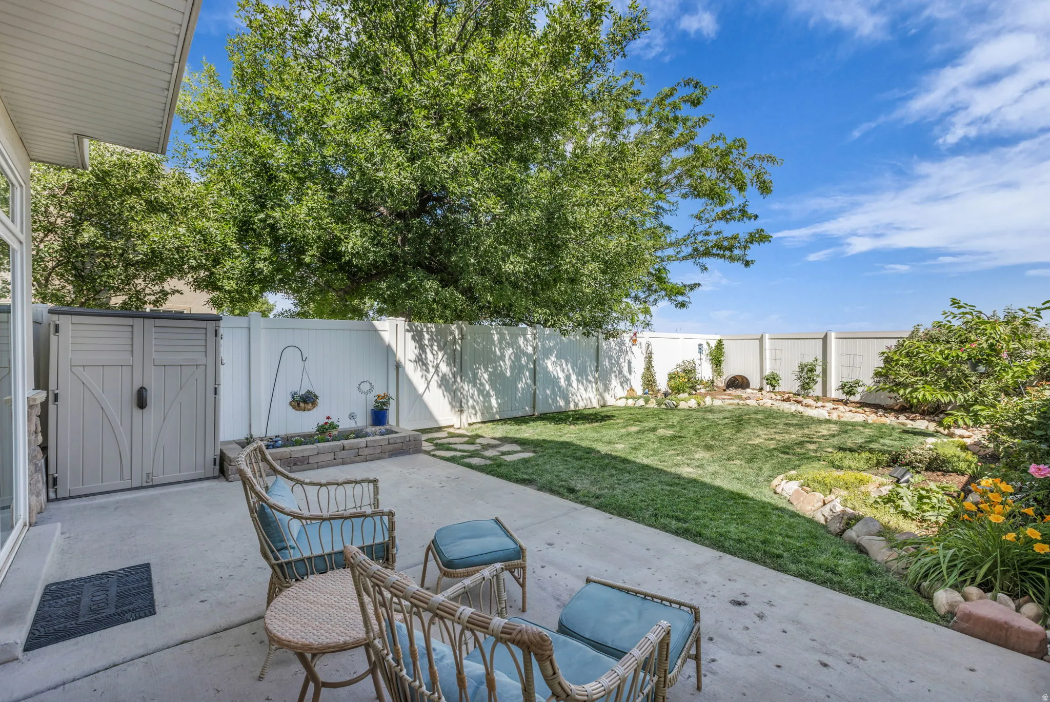 Spacious patio area with a concrete surface, a built-in storage shed, and a stone-edged planting bed