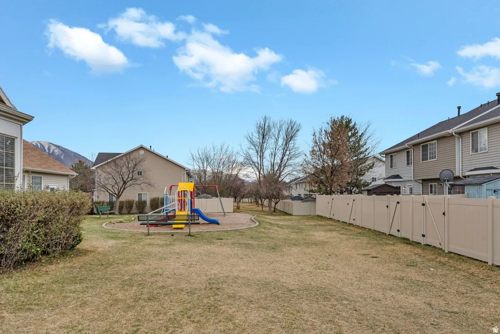 Expansive grassy area featuring a children's play structure with slides and swings, surrounded by a light-toned privacy fence
