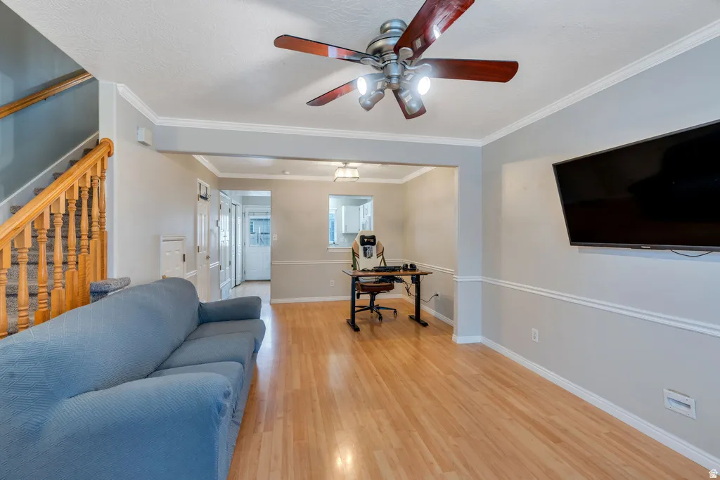 Open-concept living space with wood-finish flooring, a ceiling fan with integrated lighting, and a staircase featuring a wood banister