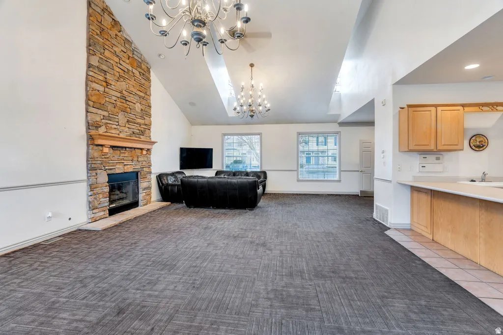 Spacious room featuring a stone-clad fireplace with a wood mantel, vaulted ceilings, and two prominent chandeliers