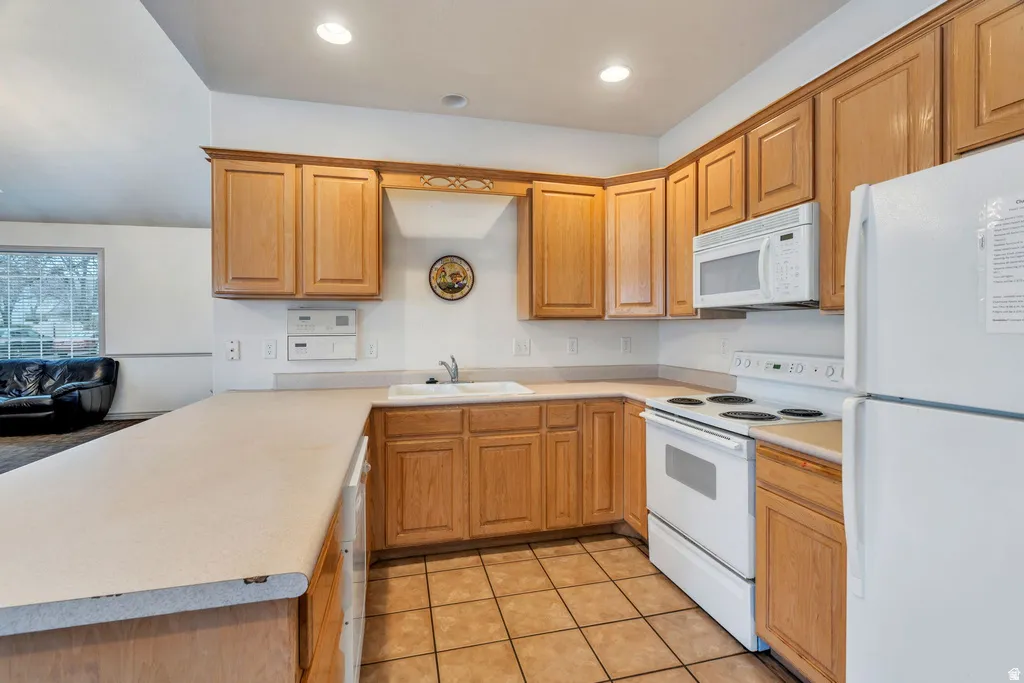 Kitchen featuring wood cabinetry, white appliances, a double basin sink, and tile flooring
