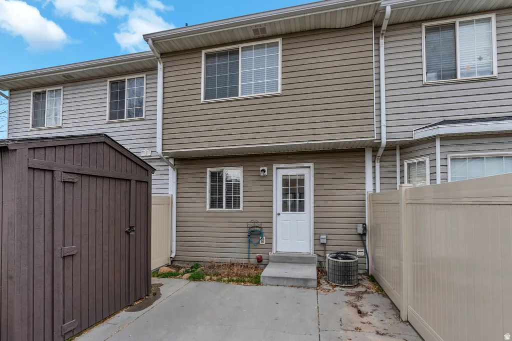 Rear exterior featuring two levels of siding, multiple windows, a white paneled door, and a concrete patio