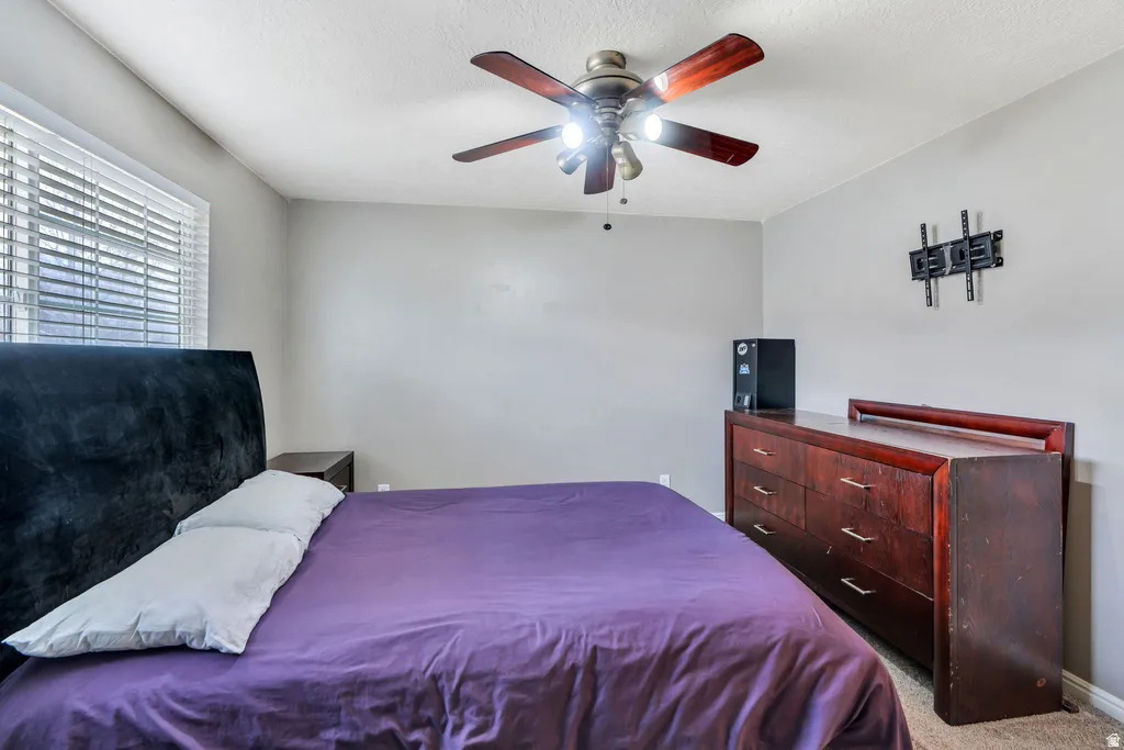 Bedroom featuring a ceiling fan with light fixture, window with blinds, and light gray wall paint