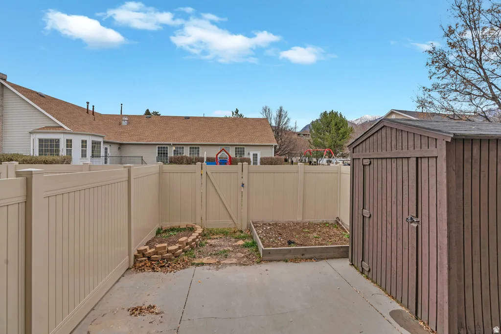 Concrete patio with a brown storage shed, raised garden beds, and a tan privacy fence with a gate