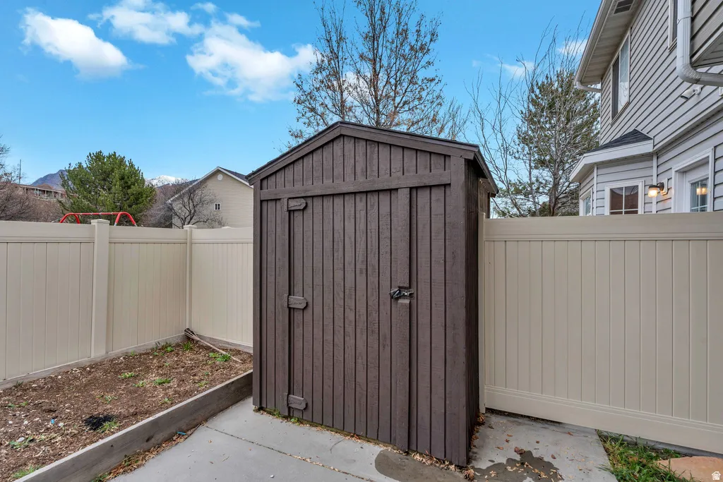 Fenced yard featuring a brown storage shed, concrete patio, and garden bed