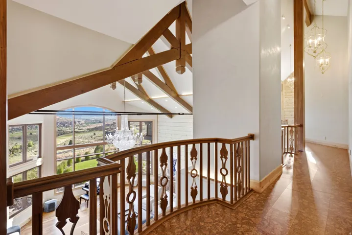 Upper-level hallway featuring ornate wood-finish railing, patterned flooring, and decorative hanging light fixtures