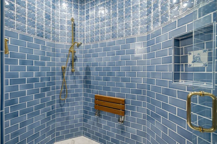 Shower with blue subway tile walls, patterned accent tile, brass fixtures, a built-in shower niche, and a wooden fold-down bench