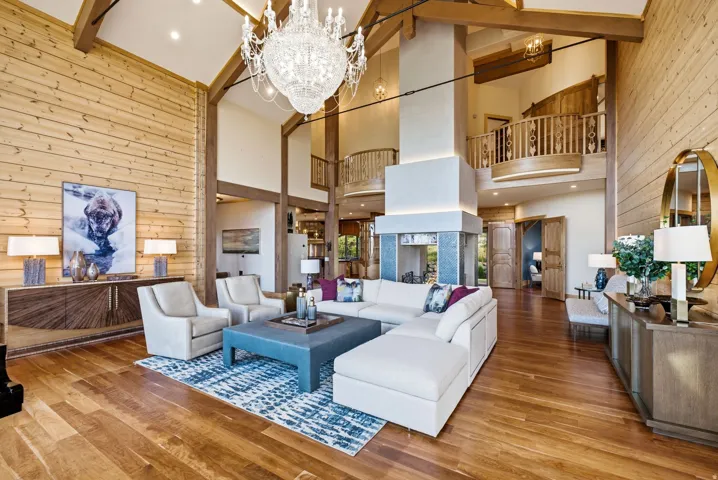 Vaulted ceiling living area featuring a prominent chandelier, exposed ceiling beams, wood-finish flooring, a central fireplace, and a second-story balcony