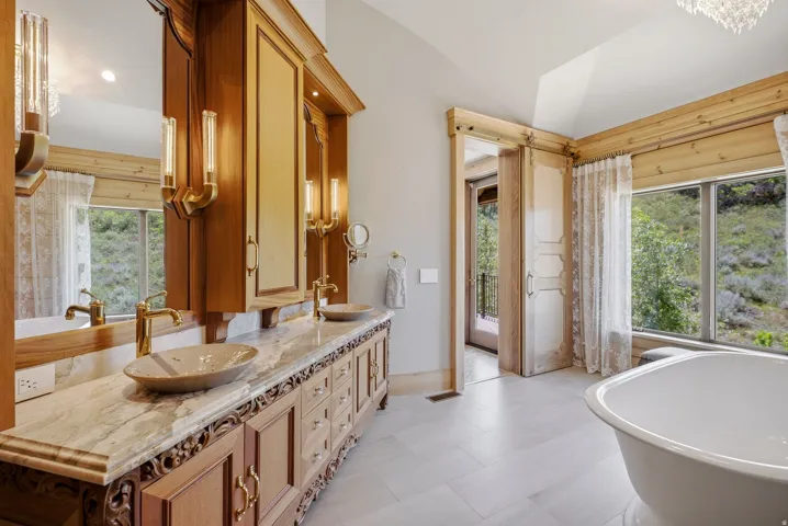 Spacious bathroom featuring a dual vanity with carved wood cabinetry, marble-finish countertop, and vessel sinks