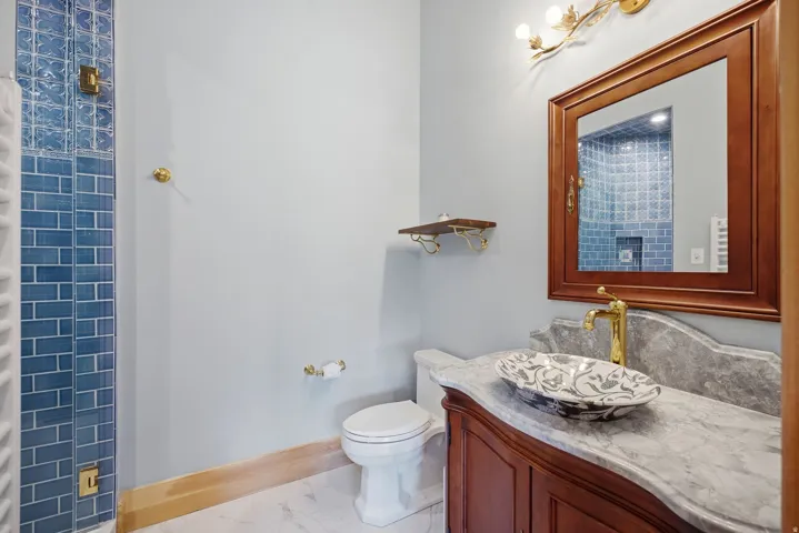 Bathroom featuring a vanity with a patterned vessel sink, gold-tone faucet, and a stone countertop