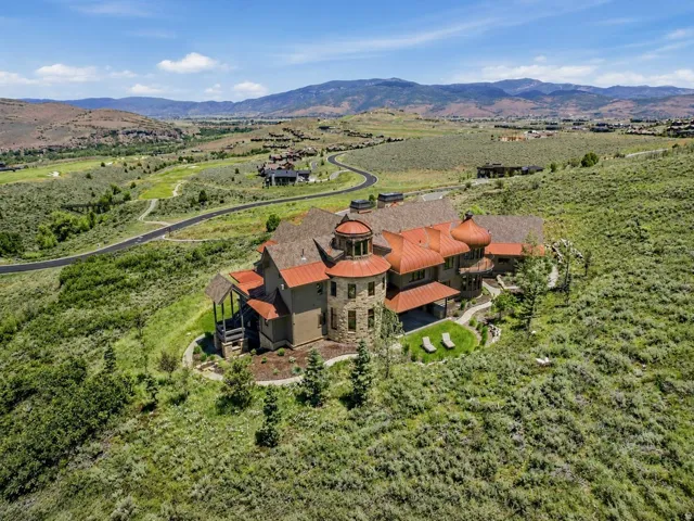 Stone and stucco exterior featuring a prominent circular turret with a domed copper roof, multiple additional copper-domed roof sections, a pitched shingle roof, and a stone retaining wall